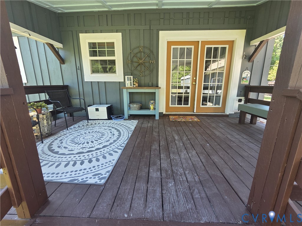 Covered wooden deck featuring board and batten siding, glass-paneled double doors, and a multi-pane window