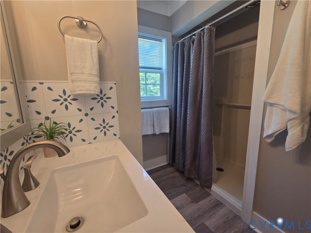 Bathroom featuring a vanity with a white countertop, patterned tile backsplash, integrated sink, metal faucet, and a shower stall with wood-finish flooring