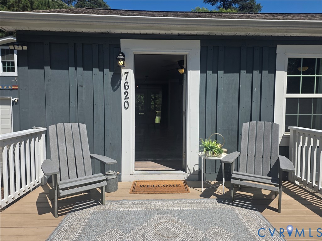 Board and batten charcoal siding, crisp white trim, exterior wall-mounted light fixture, and wooden deck with white railing