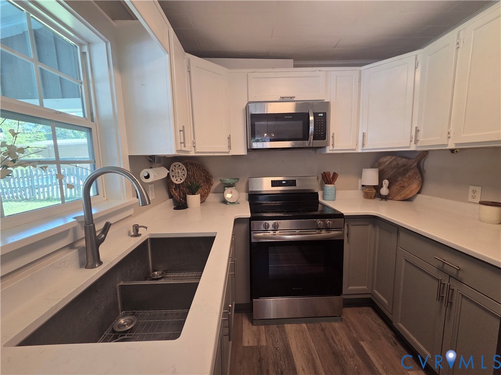 Kitchen featuring two-tone shaker cabinetry, quartz countertops, stainless steel appliances, dual-basin undermount sink with a gooseneck faucet, and wood-finish flooring