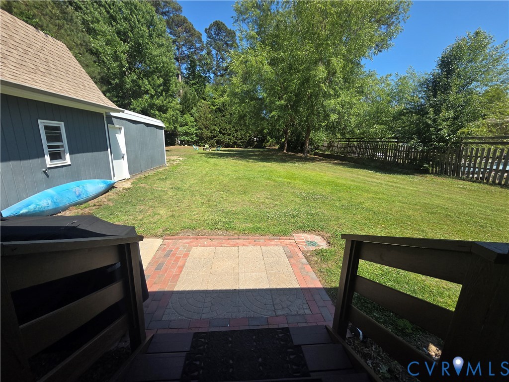 Expansive backyard featuring a grass lawn, paved brick and stone patio, wood-railing staircase, and perimeter wood fencing