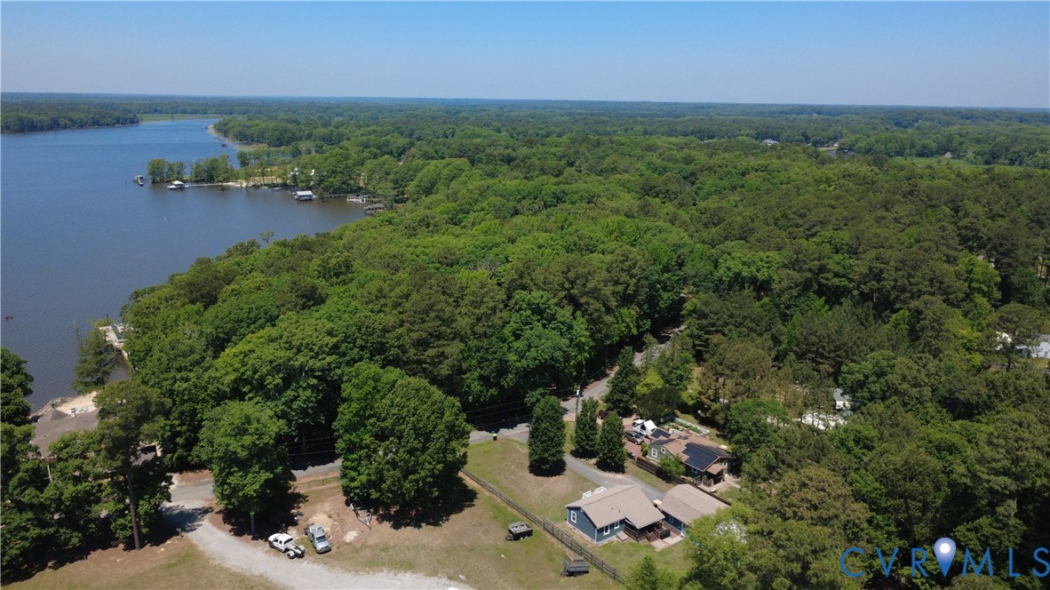 Aerial perspective featuring expansive waterfront positioning, mature forest canopy, and a gravel drive