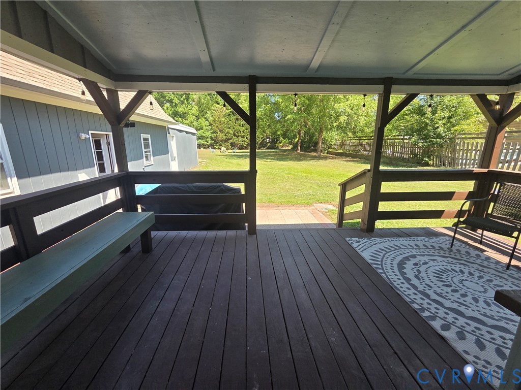 Covered wooden deck featuring a built-in bench, railing, and direct access to the rear yard