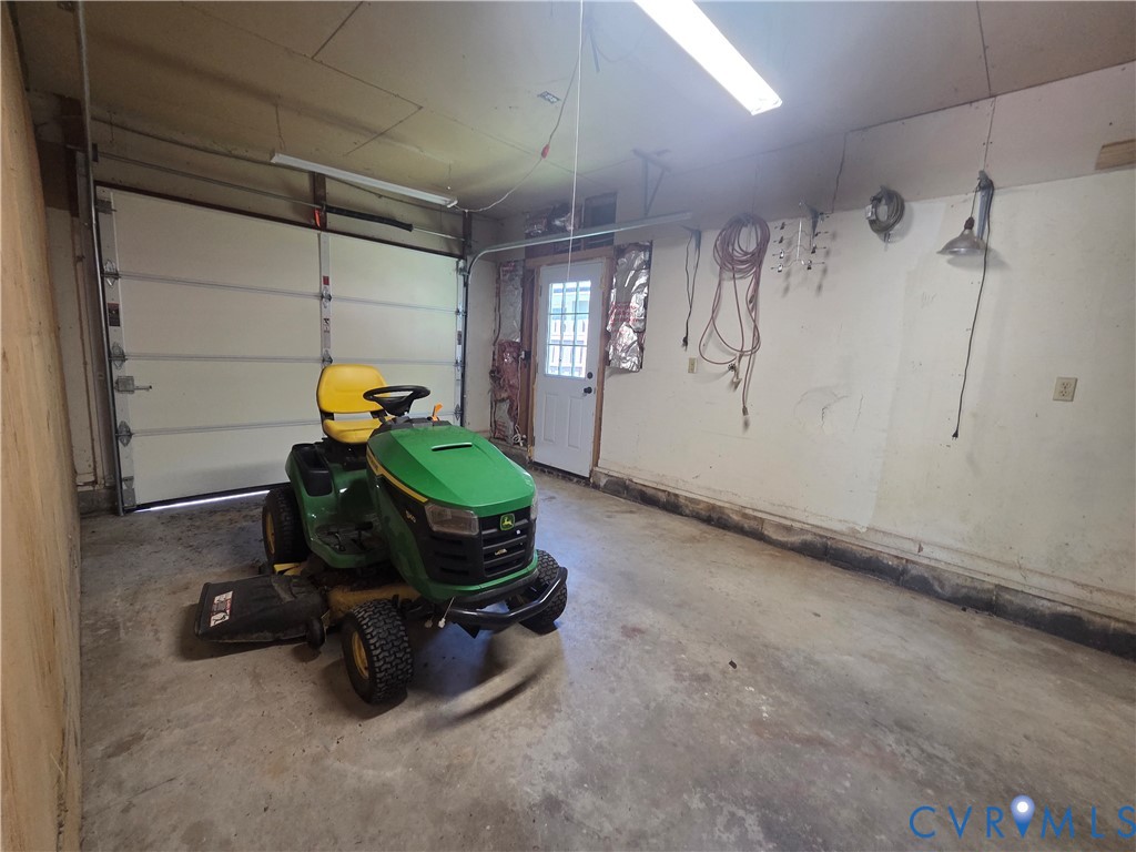 Garage space featuring a concrete floor, sectional overhead door, exterior-access door with a glass inlay, and interior wall-mounted lighting