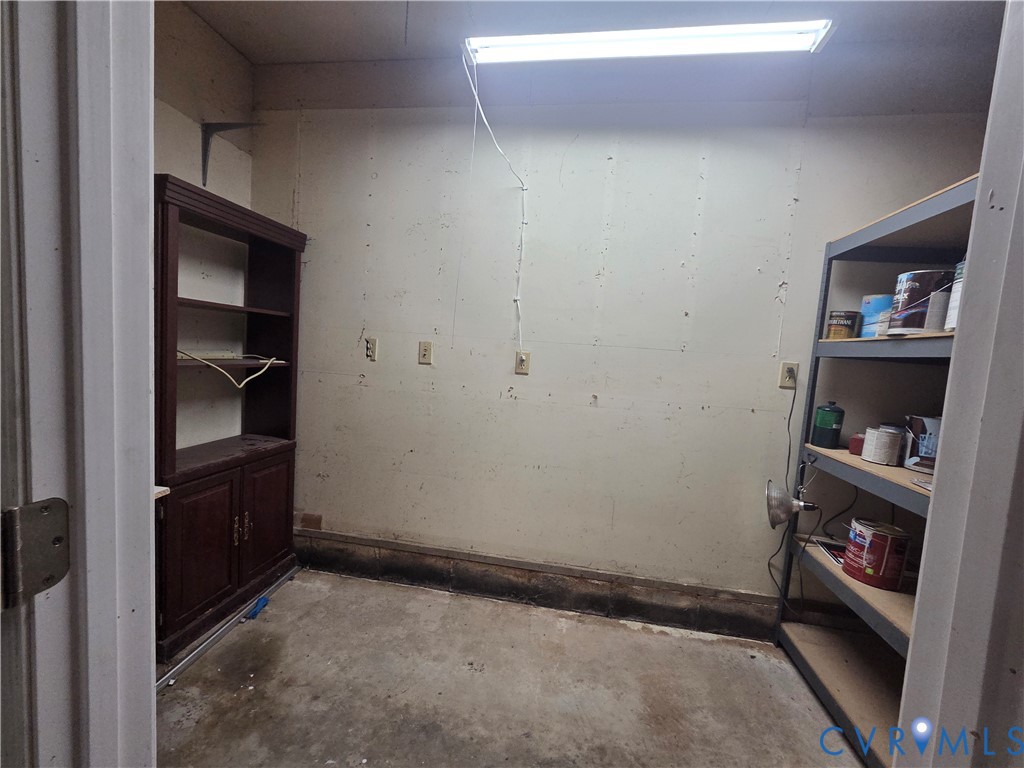 Utility space featuring concrete flooring, built-in dark wood cabinetry, and overhead fluorescent lighting