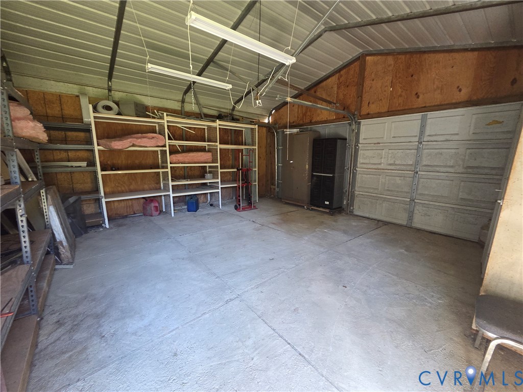 Detached garage featuring a concrete floor, plywood wall paneling, overhead fluorescent lighting, and a metal roll-up door