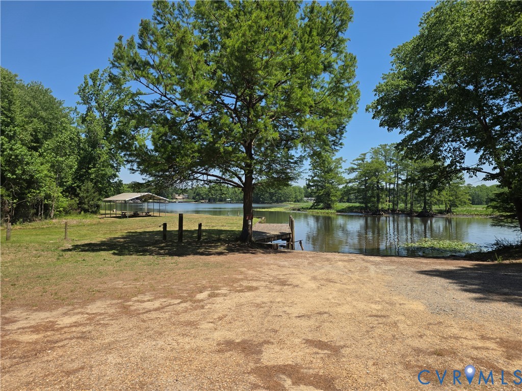 Waterfront lot featuring a private pier, mature shade trees, gravel access, and a metal-roofed pavilion