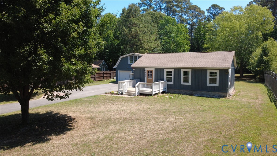 Vertical board-and-batten siding, white-railed entrance deck, asphalt shingle roof, paved driveway, and detached barn-style garage