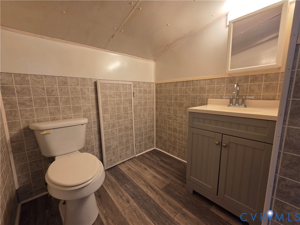 Bathroom featuring wood-finish flooring, tiled walls, vanity cabinet with integrated sink, and wall-mounted medicine cabinet