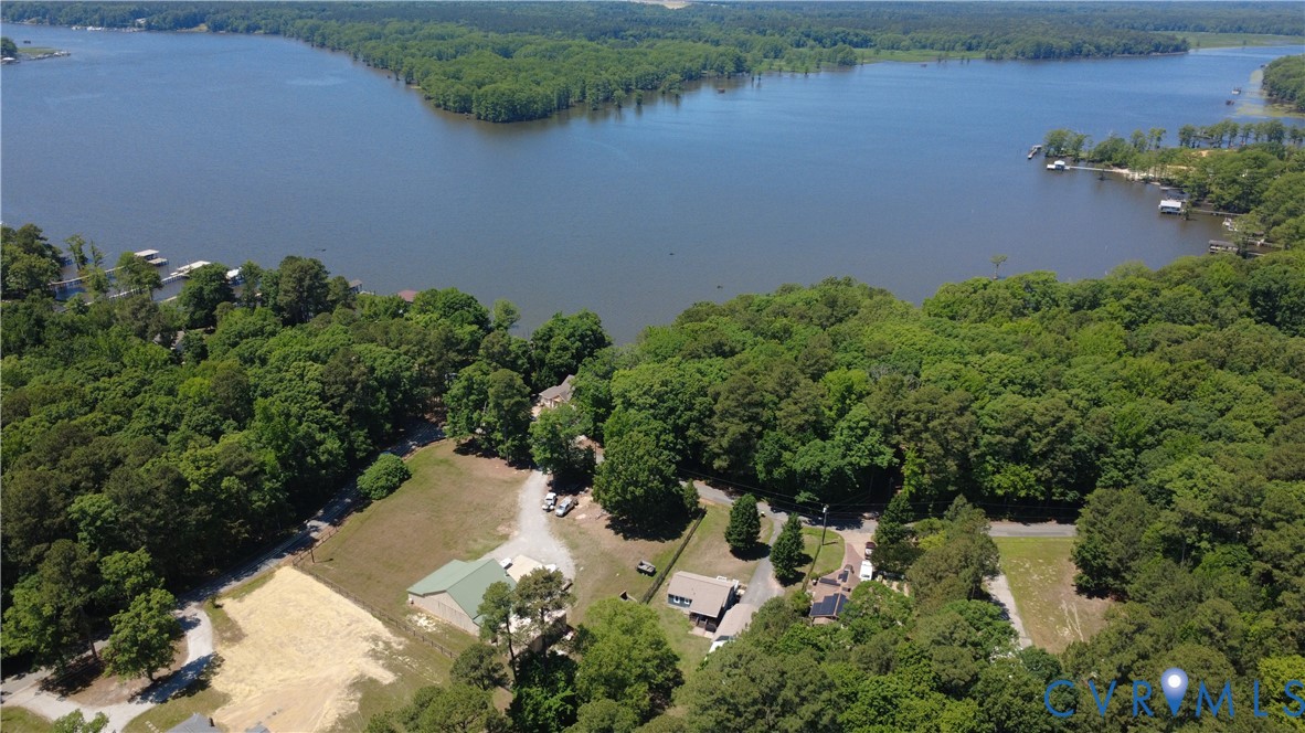 Aerial perspective of a waterfront property featuring extensive shoreline, dense perimeter woodlands, open clearing, and gravel access driveway