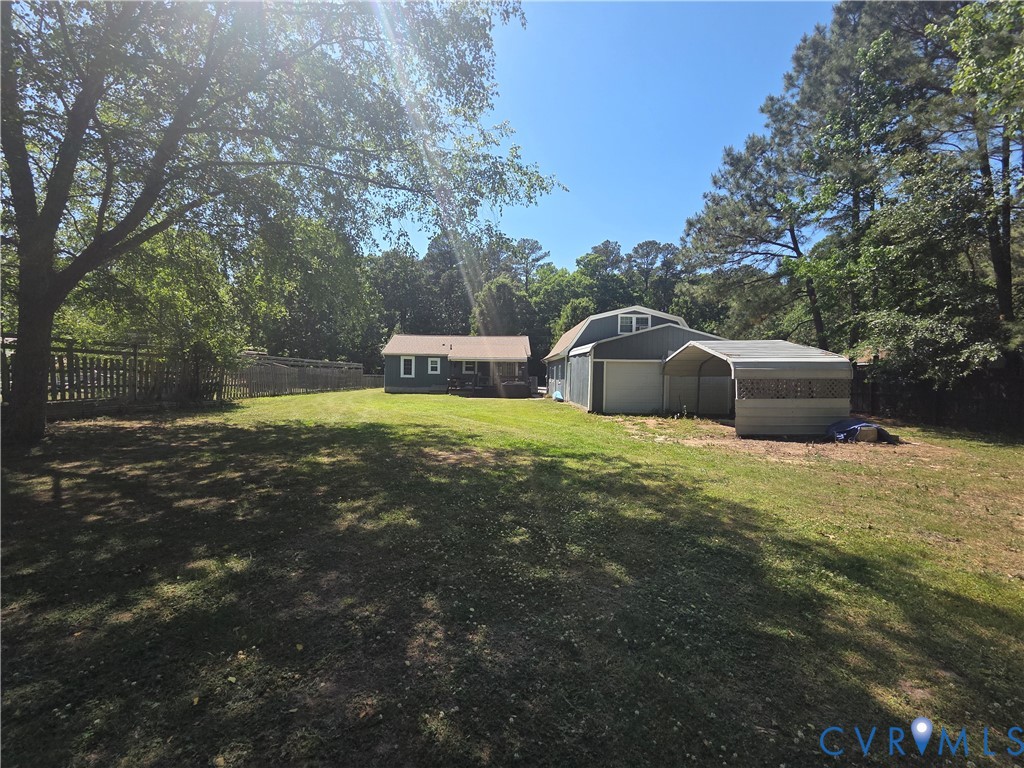 Expansive backyard featuring mature trees, a fenced perimeter, a detached two-story garage, and a metal carport