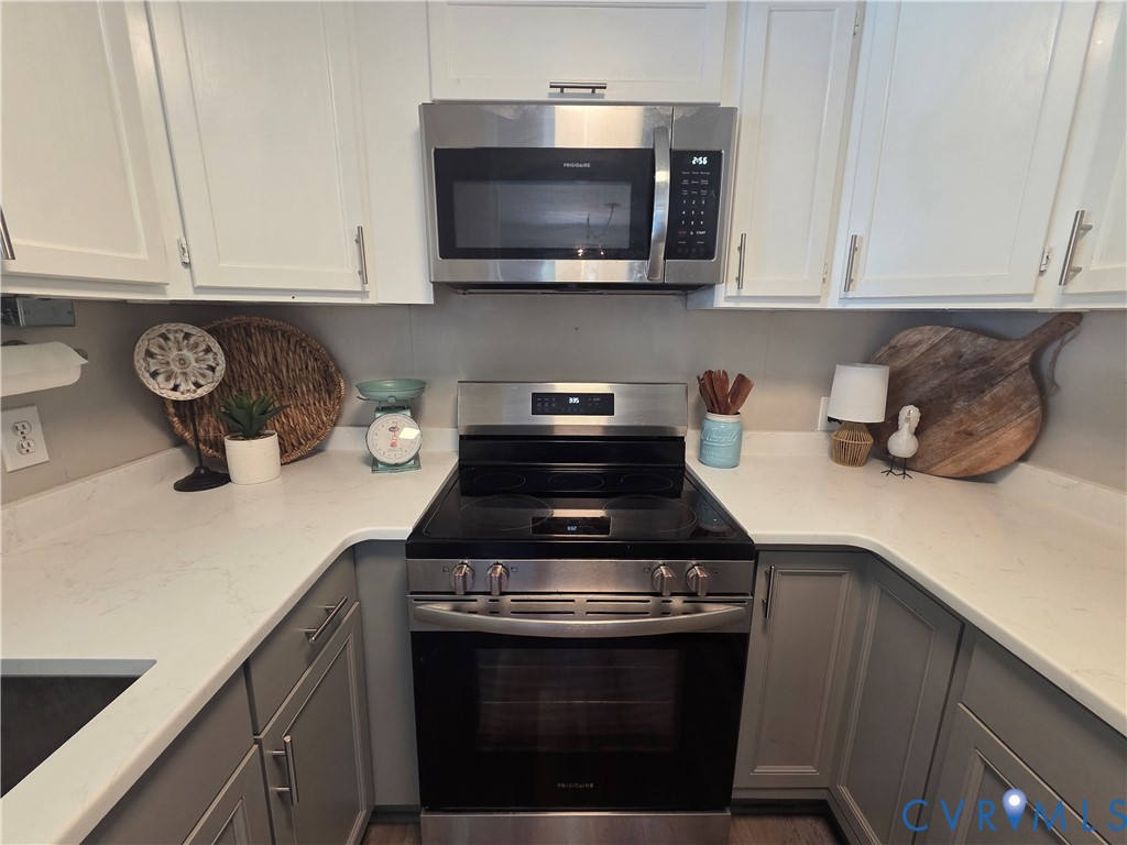 Kitchen featuring stainless steel appliances including a range and over-the-range microwave, white countertops, and two-toned cabinetry with satin nickel pulls