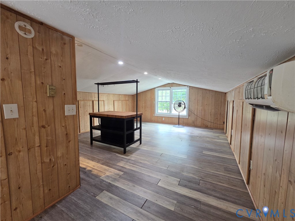 Vaulted ceiling featuring recessed lighting, wood-paneled walls, wood-finish flooring, and a wall-mounted ductless air conditioning unit