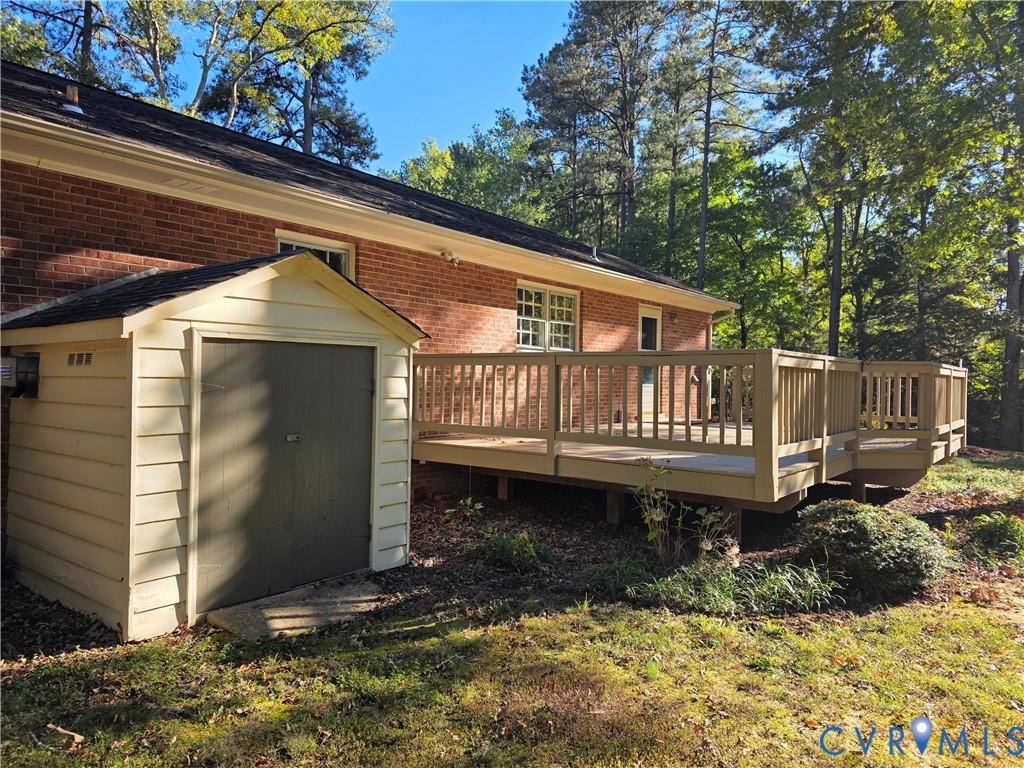Exterior featuring a brick facade, elevated wooden deck with railings, and an attached storage shed