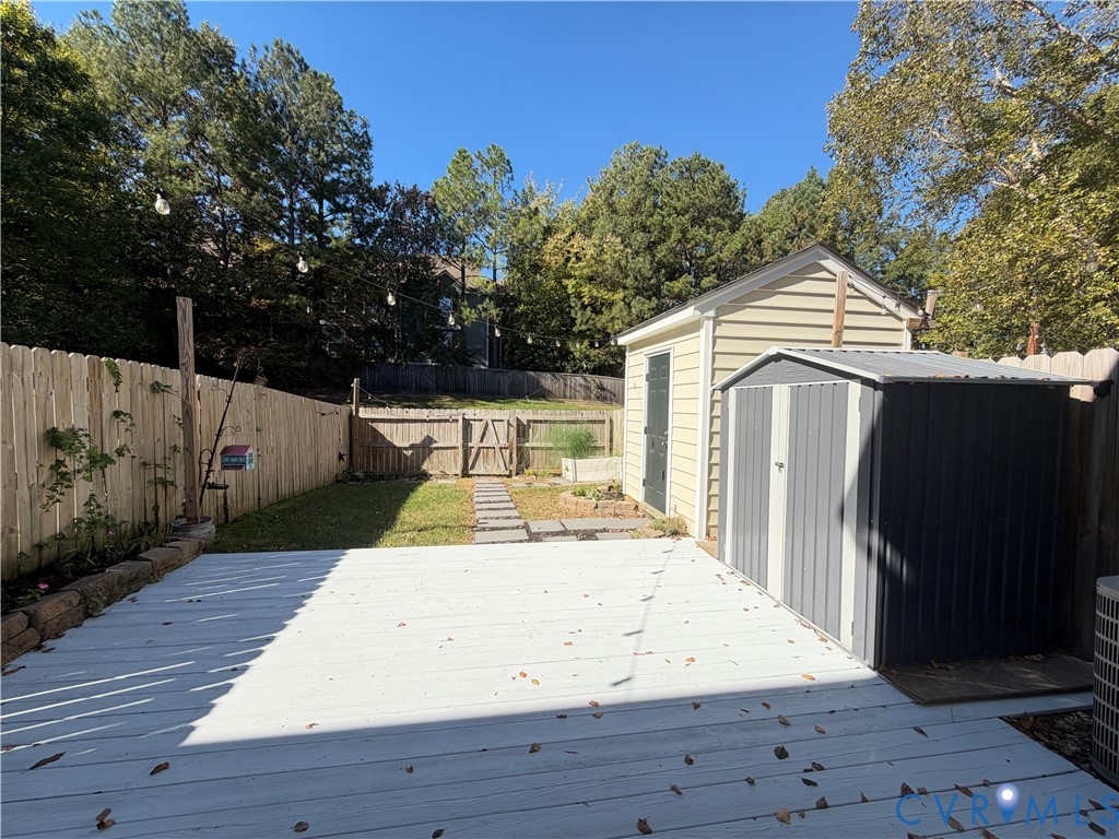 Fenced backyard featuring a painted deck, stone paver pathway, elevated garden bed, and two detached storage structures