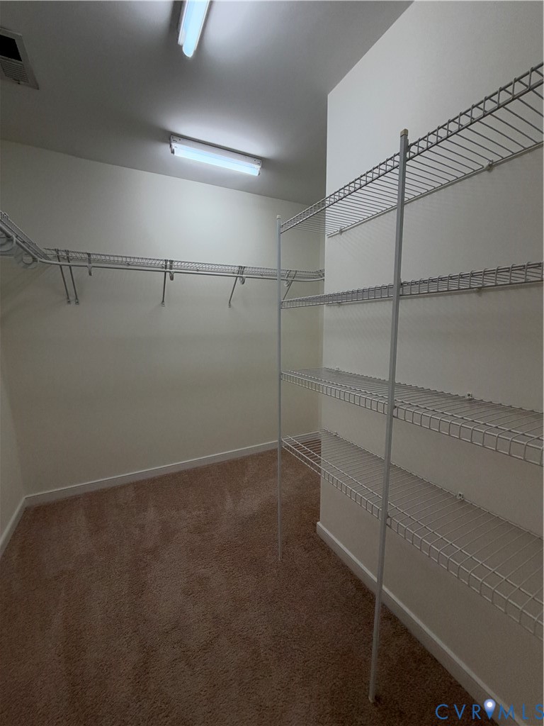 Walk-in storage space featuring neutral carpeting and tiered white wire shelving