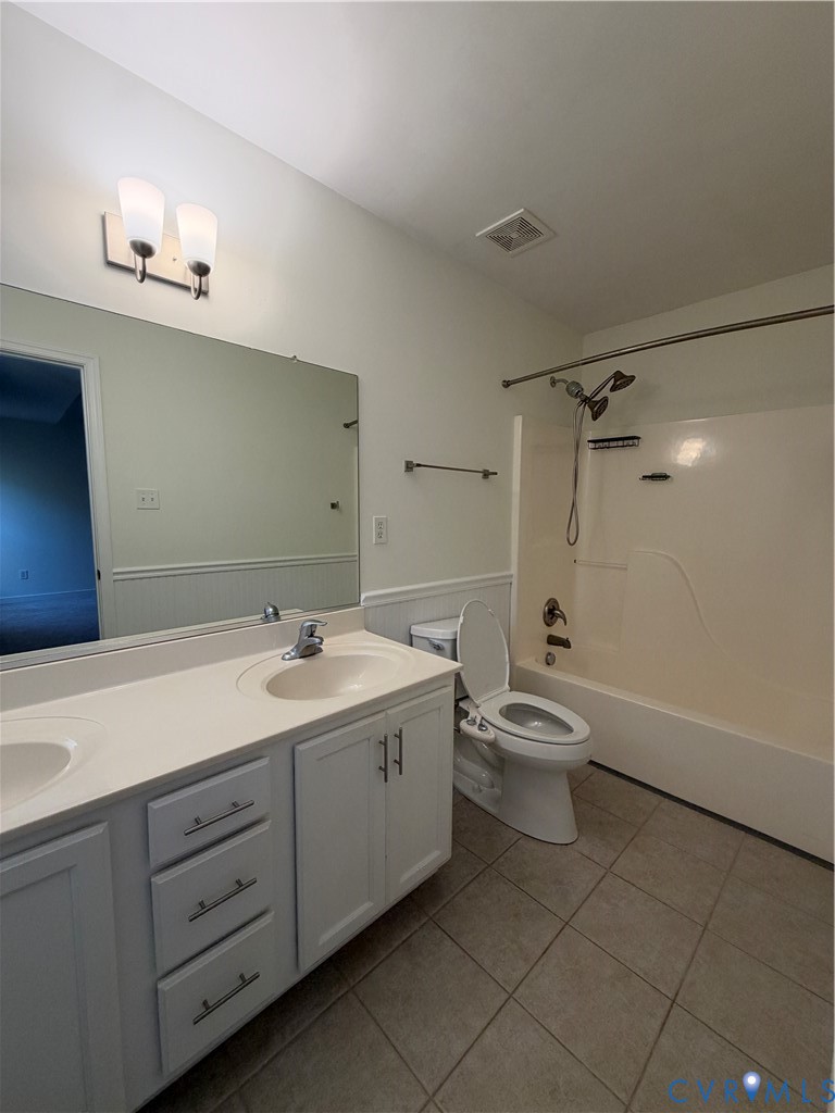 Double-sink vanity with a solid-surface countertop, tiled flooring, wall-mounted light fixture, and a full-width mirror