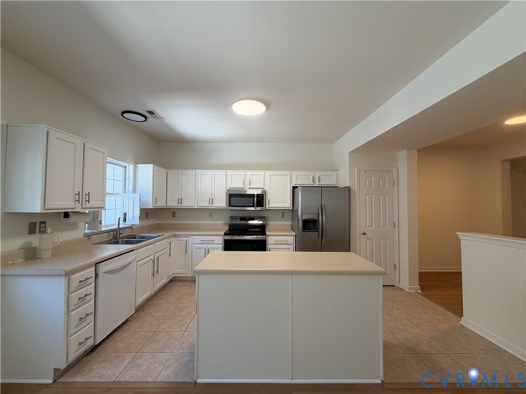 Kitchen featuring white cabinetry, center island with stone-finish countertop, dual-basin stainless steel sink, tile flooring, and stainless steel appliances