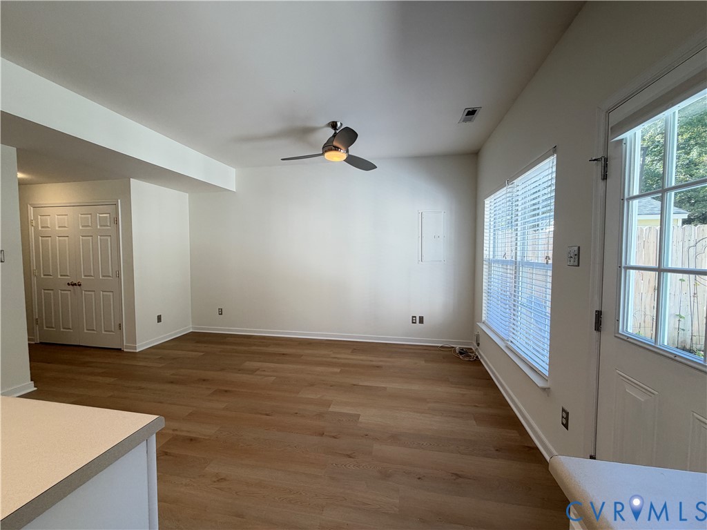 Interior space featuring wood-finish flooring, a ceiling fan with integrated lighting, dual-pane windows with horizontal blinds, and a paneled door with glass inlay