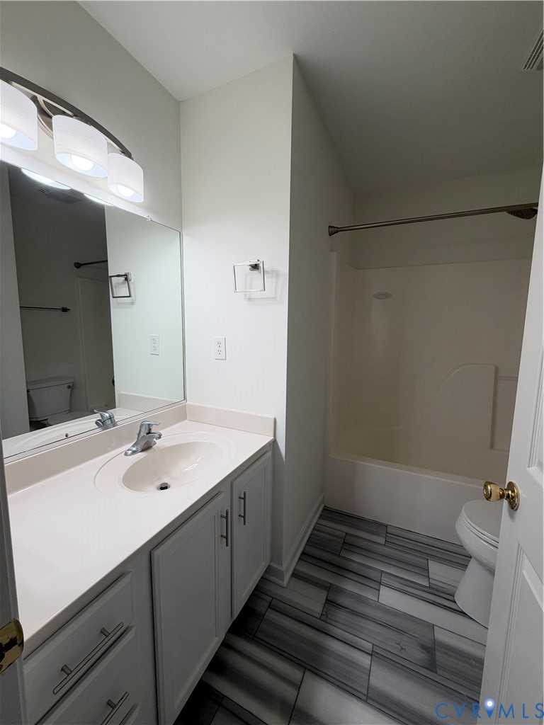 Bathroom vanity with integrated sink, stone-finish countertop, multilight vanity fixture, and full-width mirror, featuring wood-finish floor tiling and a combined tub and shower enclosure