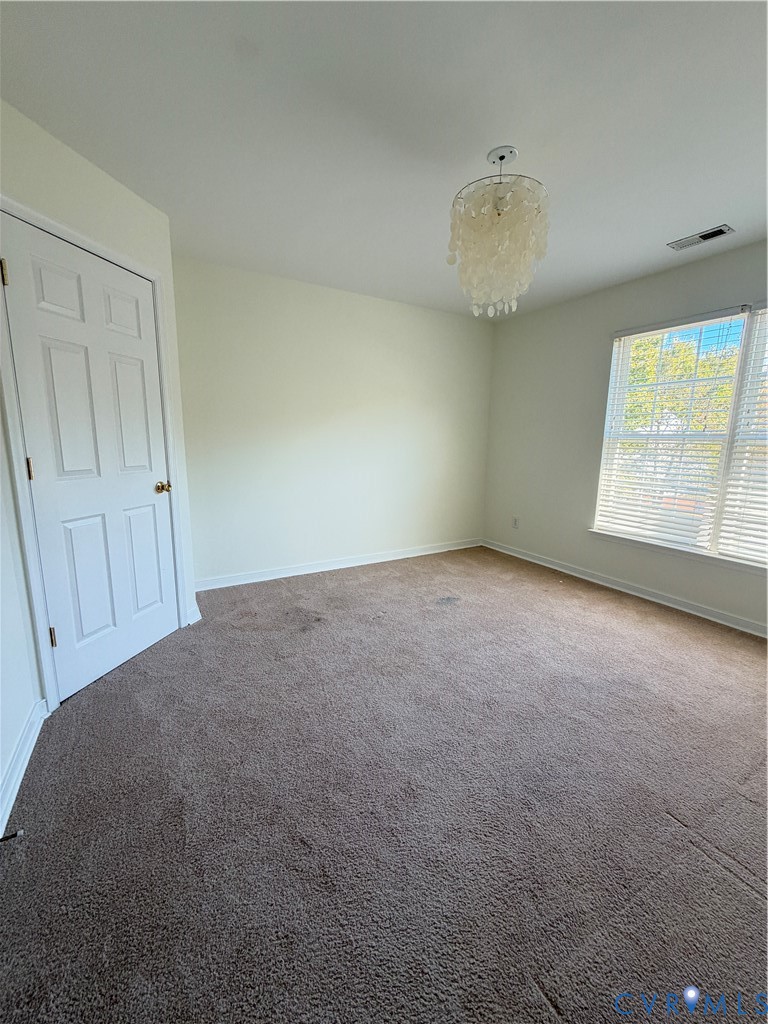 Neutral-toned interior space featuring wall-to-wall carpeting, a multi-pane window, and a decorative tiered pendant light fixture