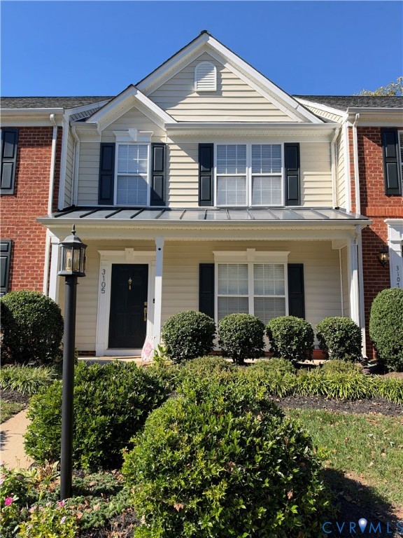 Two-story facade featuring brick and horizontal siding, a covered front porch with a metal roof, shuttered windows, and a built-in exterior lamp post