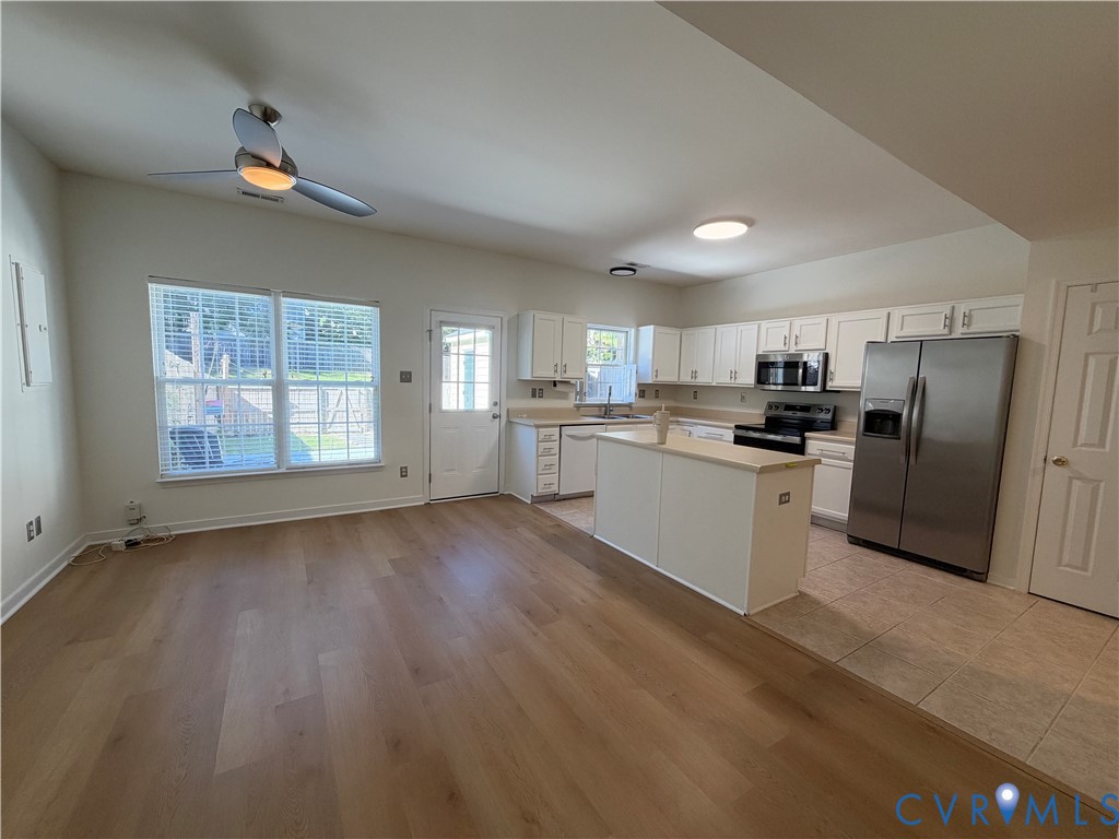 Kitchen featuring white cabinetry, an island with countertop, stainless steel appliances, wood-finish flooring, and a ceiling fan