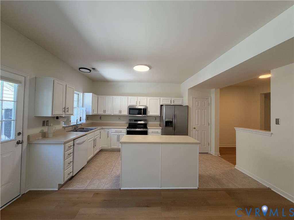 Kitchen featuring white cabinetry, center island, solid surface countertops, stainless steel appliances, and tile flooring