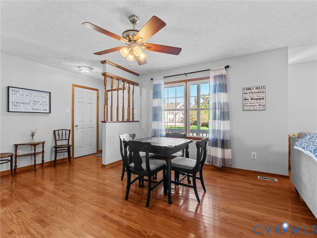 Wood-finish flooring, half-wall with wooden balustrade, multi-blade ceiling fan with integrated lighting, and multi-pane window