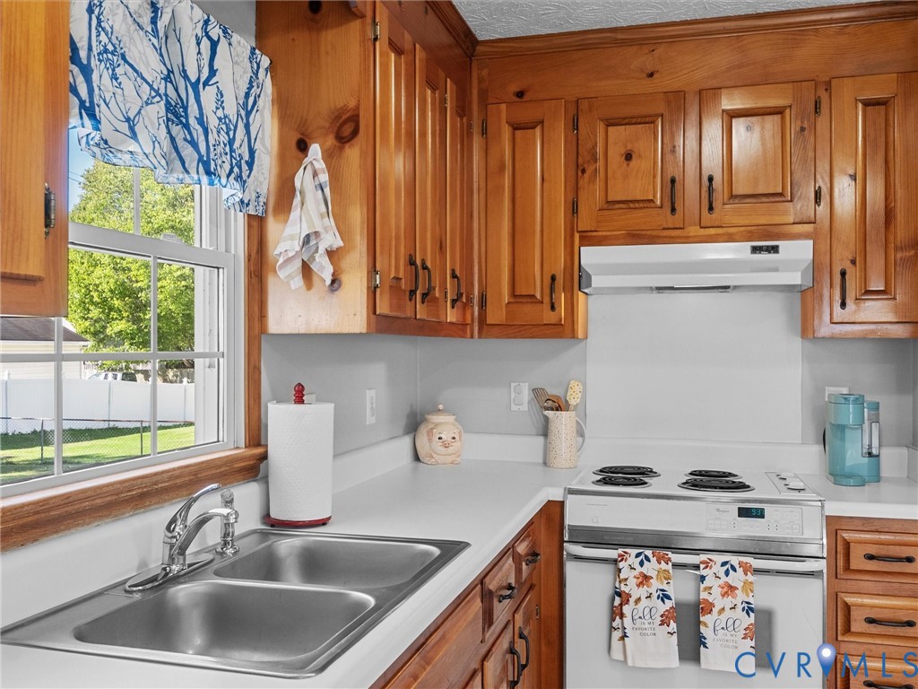 Kitchen featuring solid wood cabinetry, a dual-basin stainless steel sink with a chrome faucet, and an integrated range hood over the cooktop