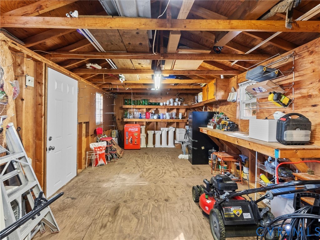 Outbuilding featuring exposed wooden rafters, plywood wall sheathing, durable plywood flooring, a solid-core entry door, and integrated built-in wooden shelving