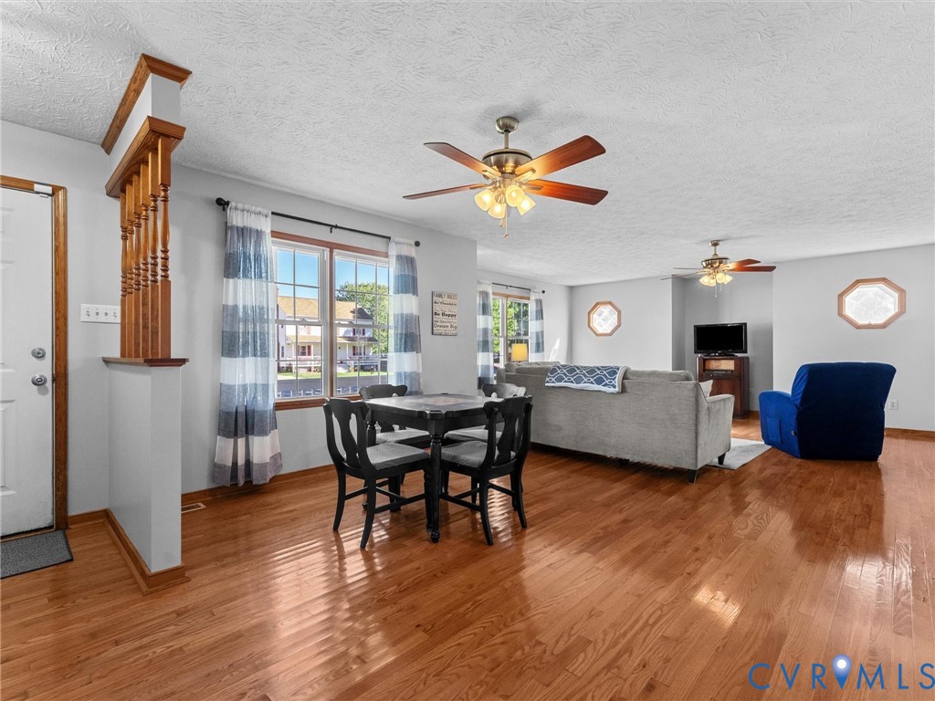 Open-concept interior featuring wood-finish flooring, half-wall spindle room divider, dual ceiling fans with integrated lighting, and multiple octagonal accent windows