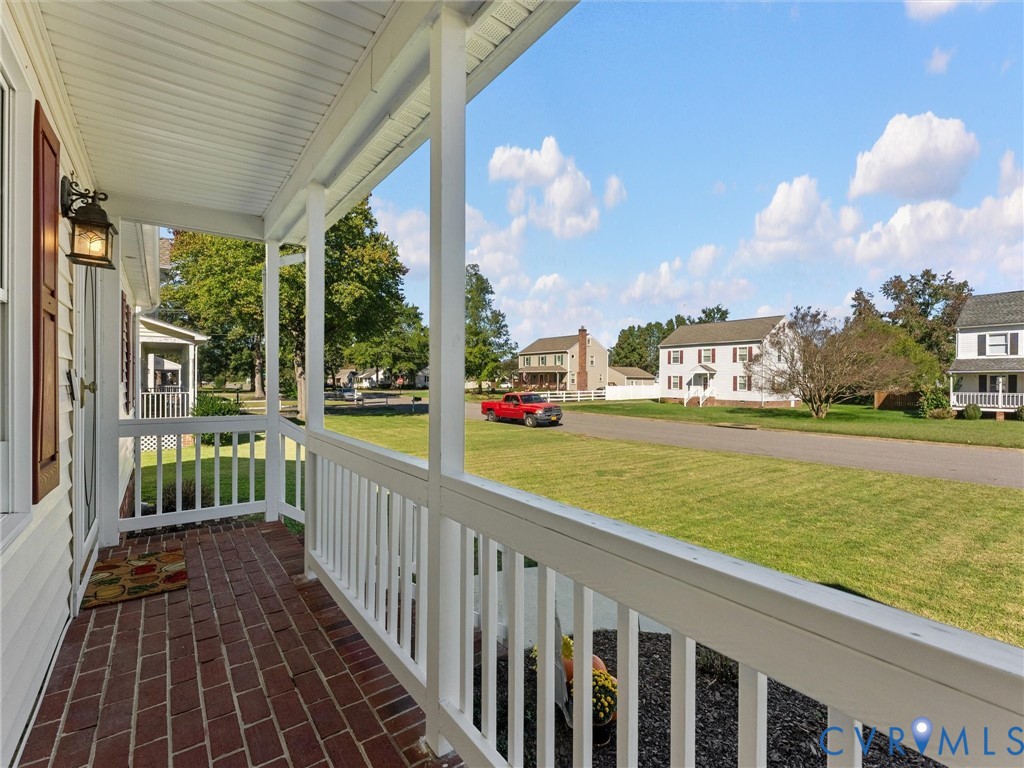 Covered front porch featuring brick flooring, white railings, and an exterior wall-mounted light fixture