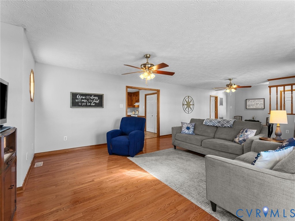 Open-concept living space featuring wood-finish flooring, dual ceiling fans with integrated lighting, and natural wood trim doorways