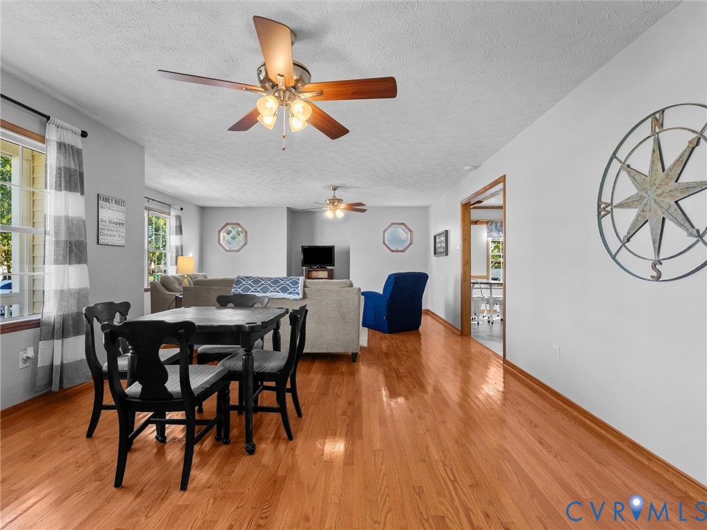 Open-concept living space featuring wood-finish flooring, dual ceiling fans with integrated lighting, and multiple windows