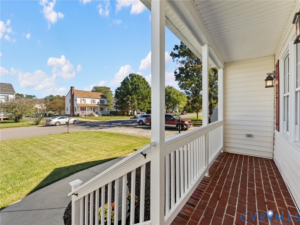 Covered front porch featuring a red brick floor, white picket-style railing, and wall-mounted exterior lighting