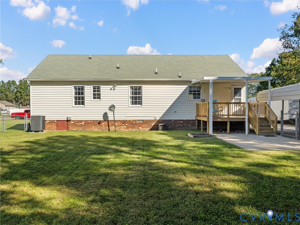 Rear exterior featuring vinyl siding, brick foundation, elevated wood deck with cover, and metal carport