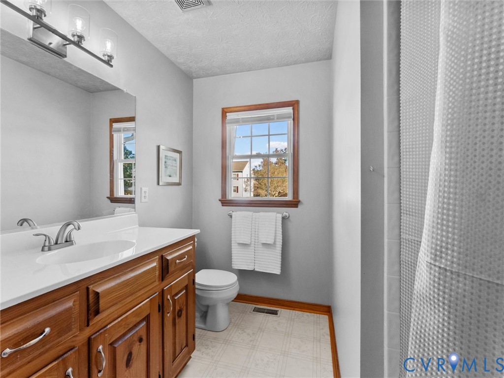 Bathroom featuring a wooden vanity with a solid-surface countertop, an integrated sink, a full-width wall mirror, and a single-hung window with wood-finish trim