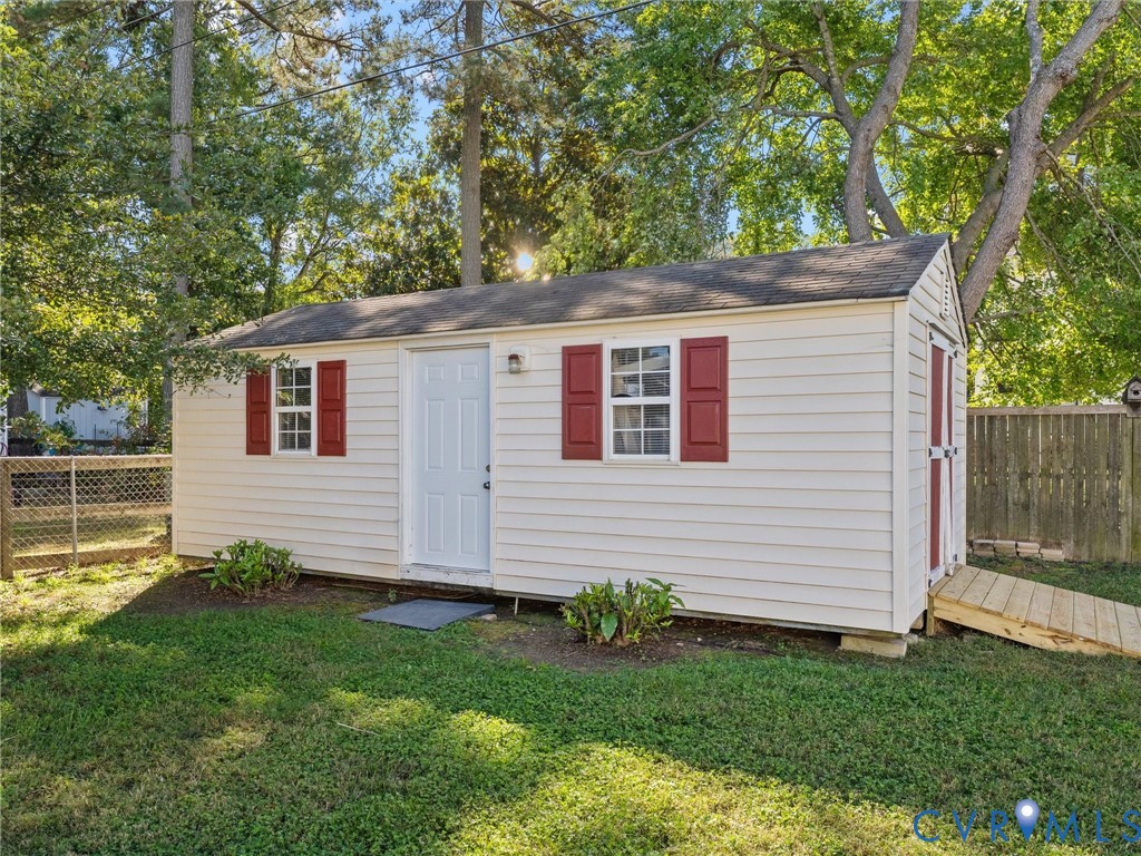 Outbuilding featuring horizontal lap siding, red shutters, a shingled roof, and an exterior wooden access ramp