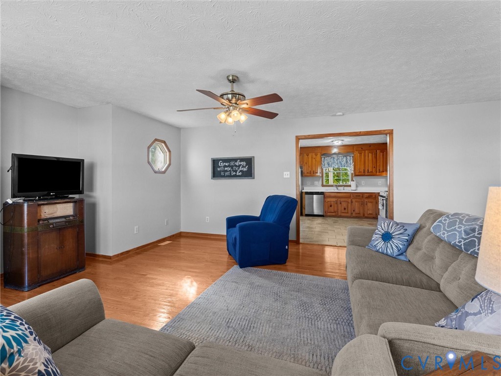 Living area featuring hardwood flooring, an octagonal accent window, and a ceiling fan with integrated light fixture