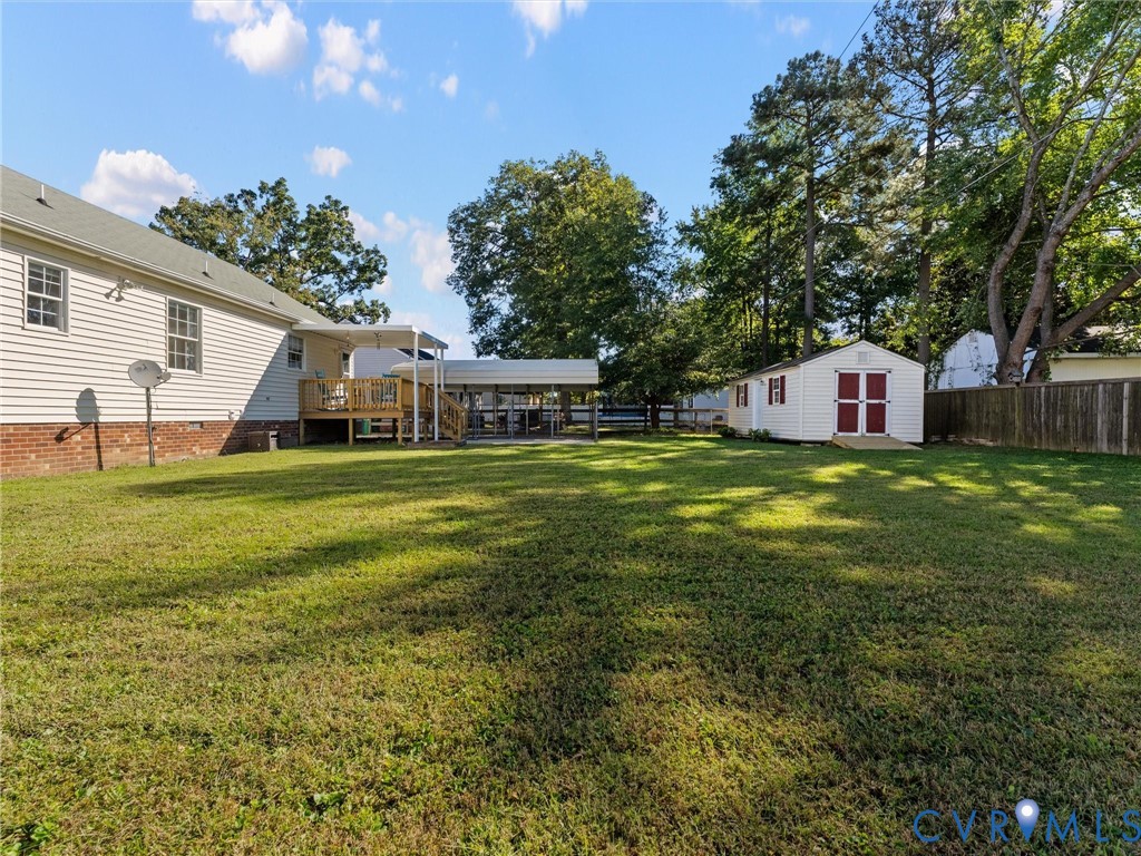 Expansive backyard featuring a leveled lawn, wood deck, detached storage building, and metal-frame carport