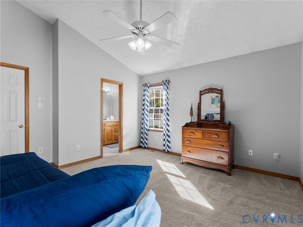 Vaulted ceiling featuring a central multi-blade ceiling fan with integrated light fixture, neutral wall finishes, and wall-to-wall carpeting