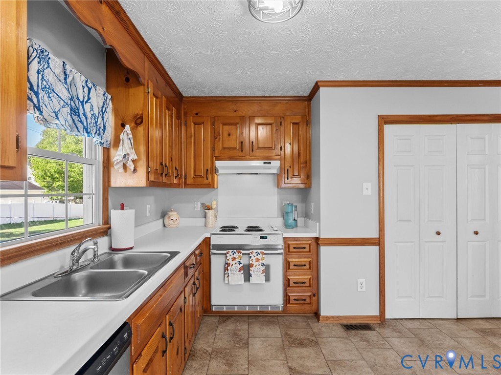 Kitchen featuring natural wood cabinetry, solid-surface countertops, dual-basin stainless steel sink, tile flooring, and bi-fold closet doors