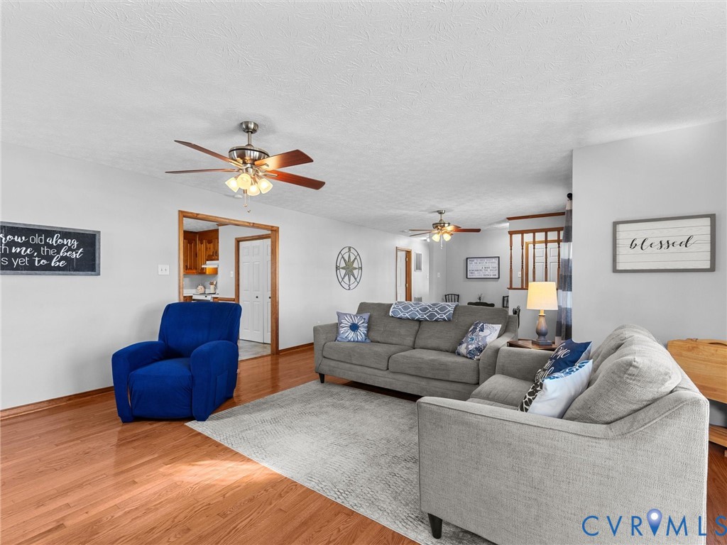 Spacious interior featuring wood-finish flooring, two ceiling fans with multi-light fixtures, and wood-toned door trim