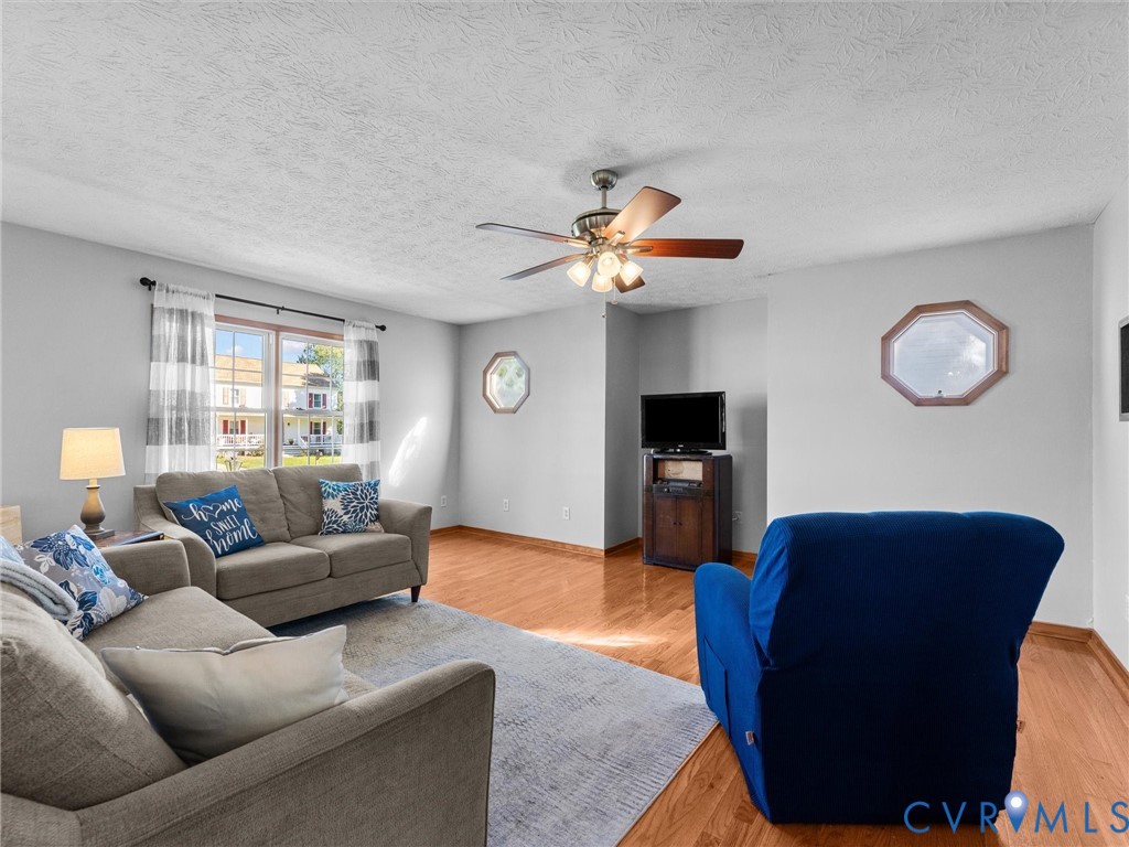 Living area featuring wood-finish flooring, a ceiling fan with integrated light fixture, double-pane window, and decorative octagonal accent windows