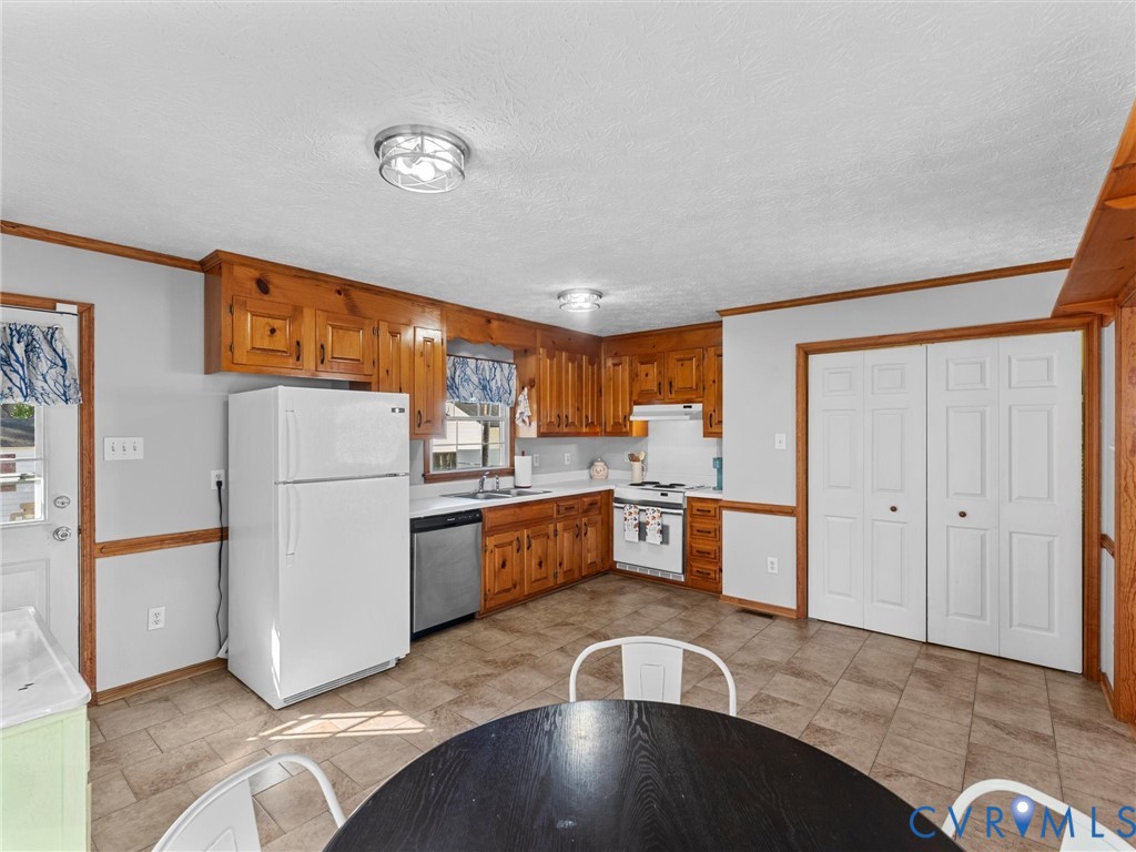 Kitchen featuring natural wood cabinetry, white appliances, tile flooring, and dual-door closet storage