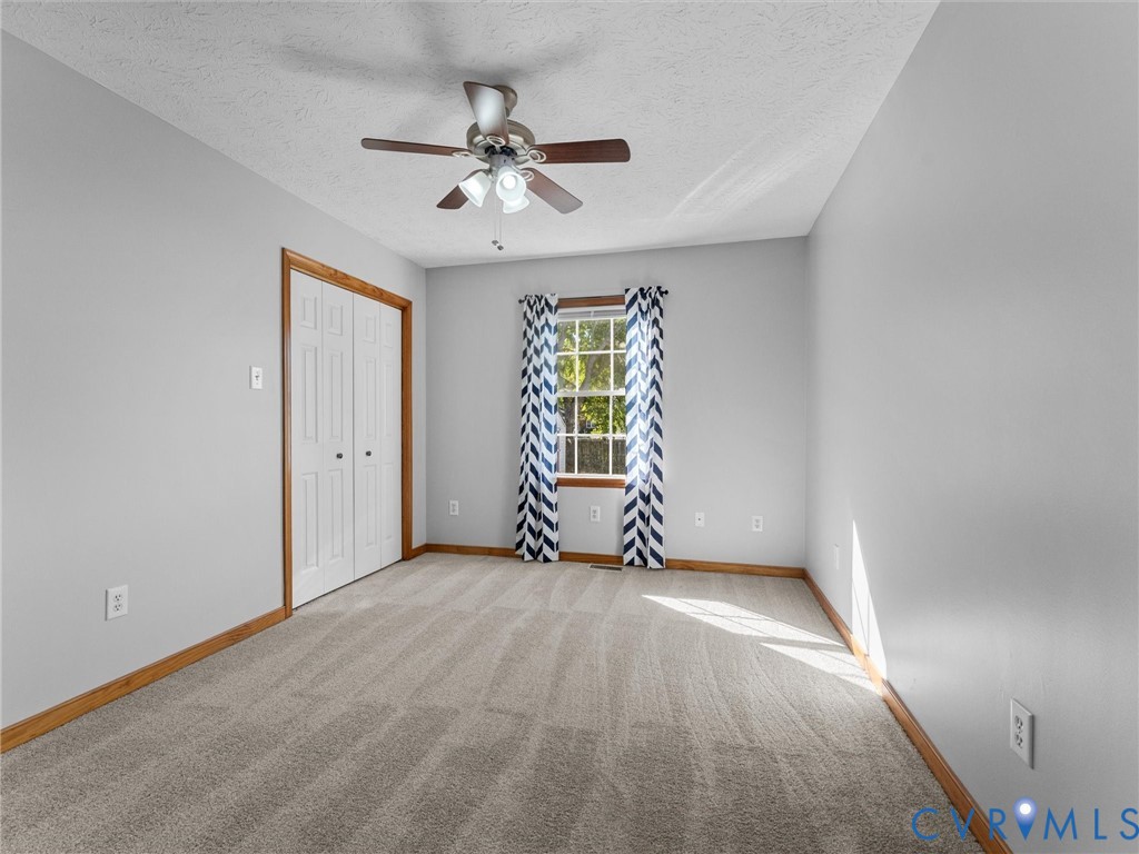 Neutral-toned carpeted flooring, wall-mounted ceiling fan with integrated lighting, dual-panel closet doors with wood trim, and a window with wood framing