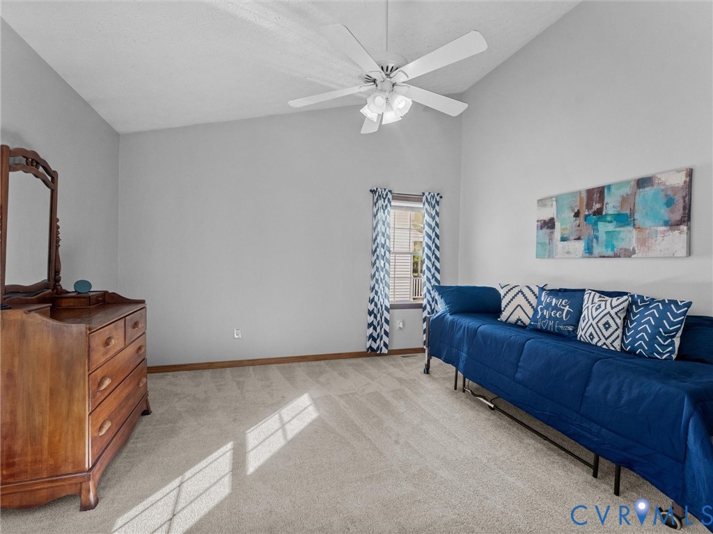 Vaulted ceiling featuring a white multi-blade ceiling fan with integrated light fixture and neutral-toned wall-to-wall carpeting