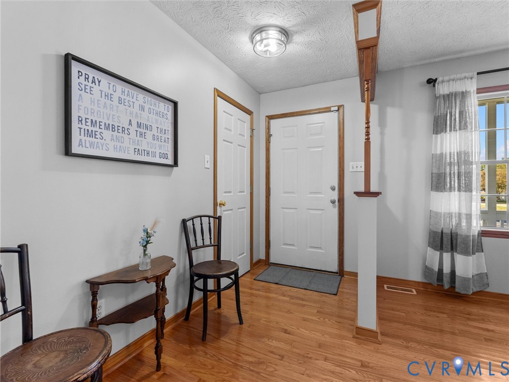 Entryway featuring wood-finish flooring, a six-panel door with wood trim, a semi-flush mount ceiling fixture, and a decorative wood column