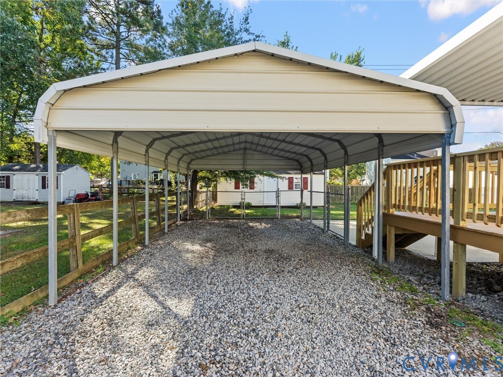 Detached metal carport featuring a gabled roof, gravel foundation, and timber perimeter fencing